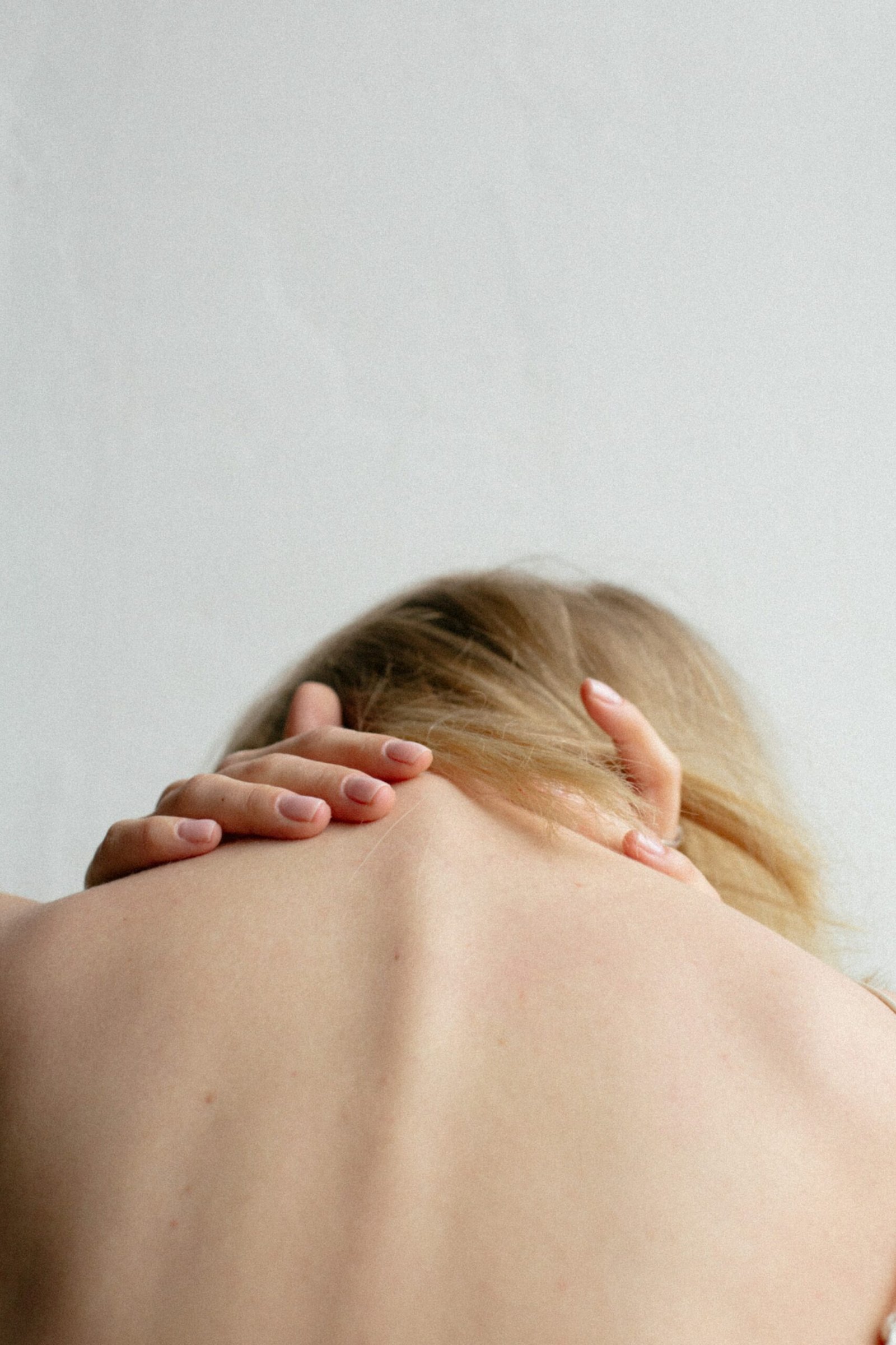 Woman's back bent over holding the back of her neck